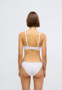 Fehér fehérnemű szett, puha, sima anyagból, állítható pántokkal és csipkés szegéllyel az alsón. Hátulnézetből.