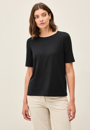 Černé tričko s krátkým rukávem a kulatým výstřihem, vyrobené z měkké látky. V kombinaci se světle zbarvenými kalhotami. Minimalistický design bez vzorů.