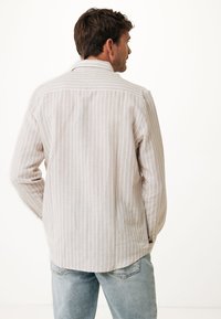 Camicia a maniche lunghe di un beige chiaro con sottili righe verticali, polsini con bottoni e orlo leggermente curvato. Realizzata in tessuto traspirante.