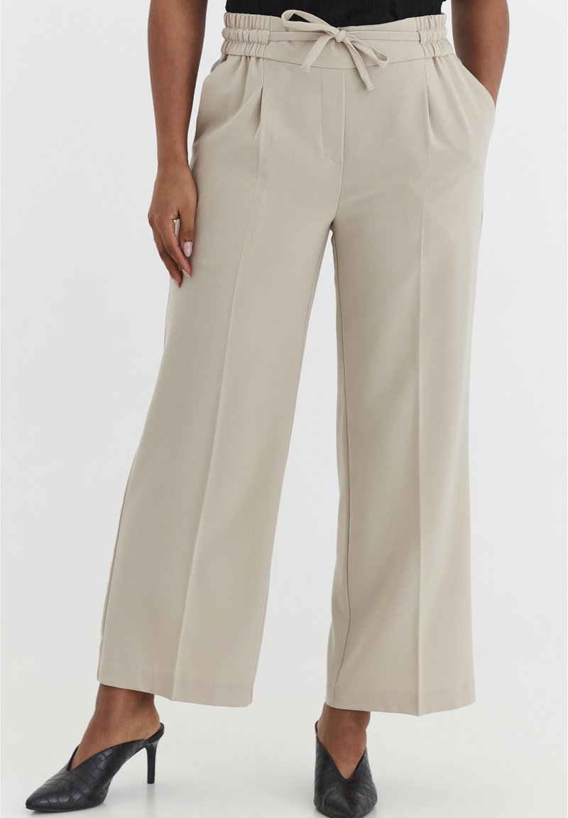 Beige wijde broek met een elastische tailleband, strikdetail en twee zijzakken. Soepele stof met een subtiele plooienontwerp.