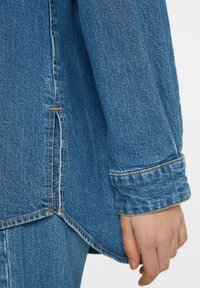 Denim shirt with a light blue color, featuring a relaxed fit, cuffed sleeves, and contrasting orange stitching along the seams and hem.