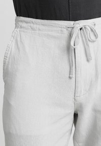 Witte, gestructureerde broek met een elastische tailleband, gedragen over een zwart top, dat het onderste torso- en heupgebied toont.