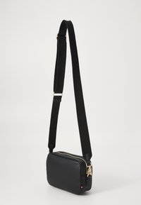 Sac bandoulière noir en cuir lisse, de forme rectangulaire, avec des accessoires en or et une large sangle en tissu réglable.