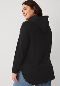 Un sweat à capuche noir avec une coupe décontractée, des manches longues et un ourlet arrondi. Fabriqué en matériau doux, il possède une capuche avec cordon de serrage et ne comporte aucun motif visible.