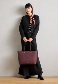 Bordeaux leren tote bag met gestructureerde afwerking, zilver hardware en lange handvatten; gecombineerd met een zwart blazer en gestreept topje.