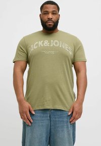 Olivgrünes Baumwoll-T-Shirt mit "JACK & JONES" in fetten, hellen Buchstaben bedruckt. Kurze Ärmel, Rundhalsausschnitt, glatte Textur, lockere Passform.