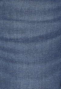 Tela de denim en azul oscuro con una textura suave, con un patrón de tejido clásico y un sutil desvanecimiento cerca del centro.