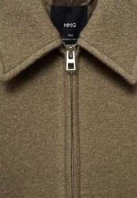 Woolowa kurtka w ziemistym odcieniu brązu, z zamkiem błyskawicznym i dużym kołnierzem. Teksturowana powierzchnia, z gładką podszewką i srebrnymi akcentami metalowymi.