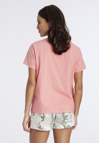 Roze katoenen t-shirt met korte mouwen, ronde halslijn en een ontspannen pasvorm. Gecombineerd met korte broeken met een bloemenpatroon in groene en gebroken witte tinten.