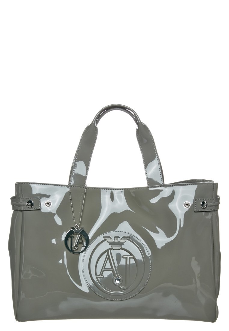 Sac à main gris brillant avec double poignées, plaque logo métallique et emblème circulaire embossé avec des lettres stylisées et détail d'aigle.