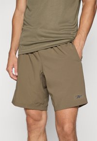 Σορτς σε ελιά πράσινο ύφασμα με απαλή υφή, διαθέτοντας ελαστική μέση και πλαϊνές τσέπες, με λογότυπο στο κάτω αριστερό πόδι.