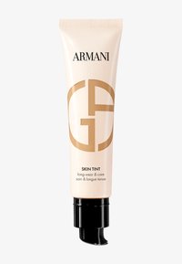 Tubo beige con bomba negra, etiquetado "Armani Skin Tint." Presenta un diseño elegante y un acabado brillante, con un logotipo dorado prominente.