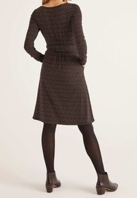 Robe noire à manches longues avec un petit motif à pois multicolores, froncée à la taille et avec une jupe évasée. Portée avec des bottines.