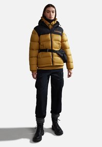 Giubbotto imbottito con corpo giallo e spalle nere, con chiusura a zip, cappuccio e una borsa a cintura nera. Abbinato a pantaloni cargo scuri e stivali neri.