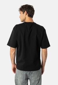 Czarna bawełniana koszulka z krótkimi rękawami, klasycznym okrągłym dekoltem i luźnym krojem. Tył jest gładki, bez zdobień.