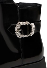 Stivaletto alla caviglia in pelle patent nera con una prominente fibbia lucida decorata con cristalli trasparenti, texture liscia e design strutturato.