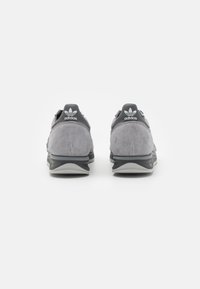 Sneakers in suede grigio con tallone e dettagli in pizzo grigio scuro. Presentano una suola imbottita e il logo Adidas sul tallone. Vista posteriore.