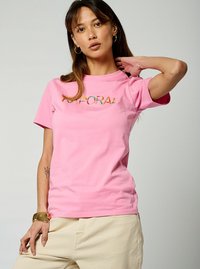 T-shirt en coton rose avec des manches courtes et un col rond, présentant un logo réfléchissant sur la poitrine et une texture douce et lisse.