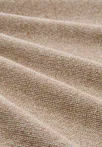 Texturiertes beige Stoff mit einem gewebten Muster, das weiche, glatte Linien und leichte Farb- und Texturunterschiede aufweist.