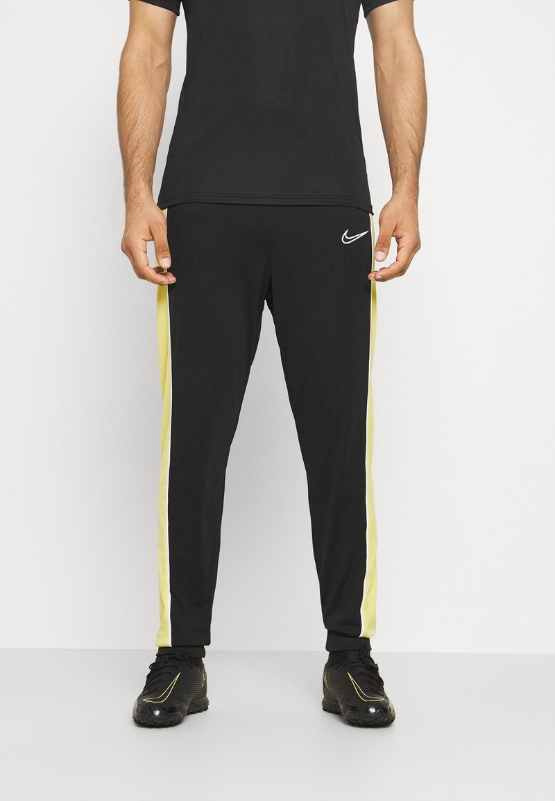 Schwarze Sporthosen mit gelben seitlichen Streifen, elastischem Taillenbund und Logo am Hüftbereich, aus einem glatten, dehnbaren Material gefertigt.