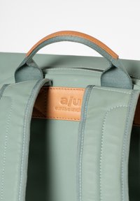 Zaino in tessuto verde con accenti in pelle. Presenta spallacci regolabili, una maniglia superiore e un'etichetta impressa con "zie e zi".