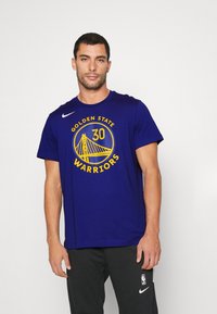 camiseta de algodón azul para hombres con un gráfico circular amarillo que lleva la frase "GOLDEN STATE WARRIORS" y un diseño de puente; mangas cortas, escote redondo.