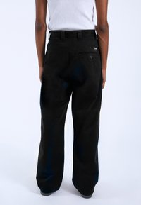 Pantalones de pierna ancha negros con una tela texturizada, que cuentan con un bolsillo trasero y pasadores para cinturón. Los pantalones tienen un corte relajado y puños ajustados.
