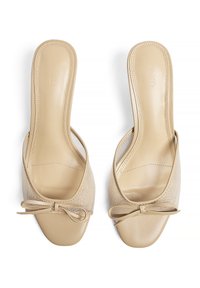 Sandales ouvertes couleur beige avec une tige en maille, un talon plat et un nœud décoratif à l'avant, agrémentées de détails en cuir lisse.