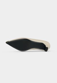 Chaussure à talon haut beige à bout pointu vue de la semelle, avec une semelle noire et un petit talon bloc.
