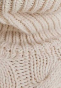 Tejido de punto en color beige claro con un patrón texturizado en zigzag que presenta secciones acanaladas alternas, añadiendo profundidad y dimensión al material.