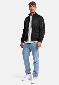 Chaqueta bomber negra con cierre frontal, dos bolsillos delanteros y puños de punto. Combinada con jeans de color azul claro y zapatillas blancas.