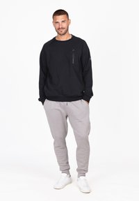 Sudadera negra con un bolsillo con cremallera en el frente, combinada con pantalones de chándal gris claro. Zapatillas blancas completan el atuendo. Adecuado, de ajuste simple y relajado.