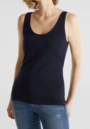 Débardeur bleu marine sans manches avec un col rond, en tissu lisse, associé à un jean déchiré bleu clair.