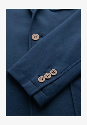 Navy blue blazer sleeve with three tan buttons, showing detailed stitching and texture of the fabric.