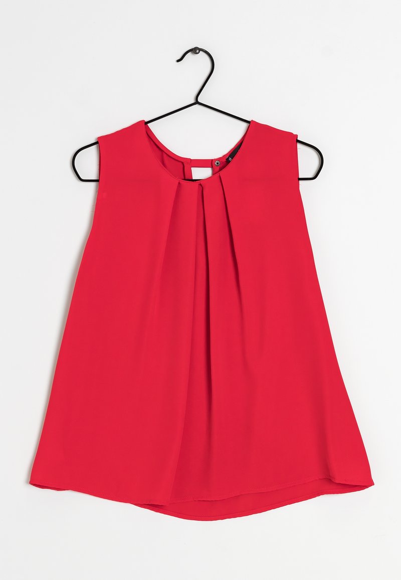 Blouse sans manches rouge en tissu léger avec un design à plis à l'avant et un col rond, suspendue à un crochet noir.