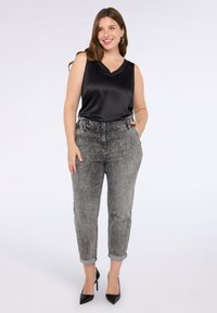 Svart satin utan ärmar topp, grå slitna jeans med utsmyckningar, uppvikta vid anklarna, kombinerat med svarta högklackade skor.