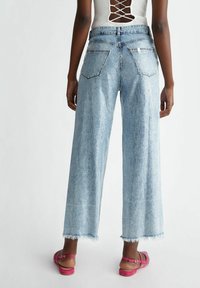 Vaaleansiniset leveälahkeiset farkut, joissa on repsottavat helmanteet, pystyribbistruktuuri ja kaksi takataskua. Yhdistetty vaaleanpunaisiin ohuisiin sandaaleihin.