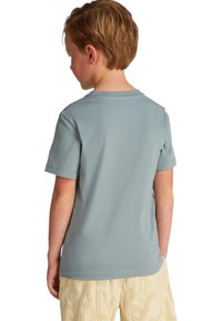 Camiseta de manga corta en tela azul clara, con cuello redondo, textura suave, vista trasera lisa, combinada con pantalones beige texturizados.
