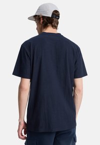 Navy blue cotton t-shirt with short sleeves and a relaxed fit. Worn with a light gray cap featuring perforated details.