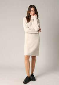 Robe tricotée beige clair avec un col montant roulé, une texture côtelée et des manches longues, associée à des baskets noires épaisses.