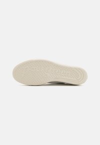 Semelle de sneaker blanche avec caoutchouc texturé présentant des motifs circulaires, un nom de marque en relief et des bords incurvés pour une adhérence et un soutien.