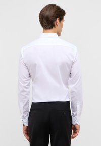 Witte lange mouw dress shirt met een rechte snit, knoopmanchetten en een subtiele glans, gecombineerd met zwarte broeken. De achterzijde heeft een klassieke kraag.