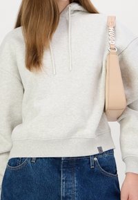 Šedá mikina s kapucí a šňůrkami, v kombinaci s modrými džínami. Obsahuje připojenou béžovou tašku s logem "HUGO" na ramenním popruhu.