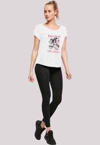 Hvit bomulls T-skjorte med kort erm som har grafisk trykk av ansikter og tekst. Kombinert med svarte leggings og svarte treningssko.
