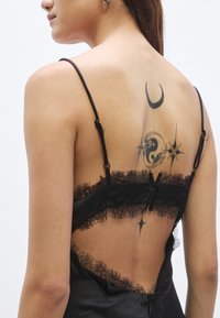 Μαύρο σατέν καμισολέ με δαντελένιο τελείωμα, ρυθμιζόμενους ιμ�άντες και κουμπιά στην πλάτη. Διακοσμημένο με τατουάζ ουράνιων σχεδίων στην πλάτη.