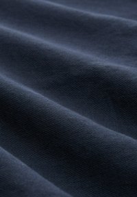 Tmavě námořnická látka s měkkým, texturovaným povrchem a viditelnými záhyby, která ukazuje hladký, ale mírně tkaný vzhled.