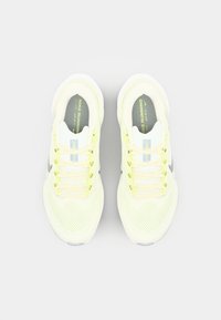 Des chaussures de course en maille jaune clair avec des accents gris. Elles disposent d'une semelle rembourrée et de lacets plats pour un ajustement sécurisé. Branding subtil sur la languette.