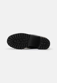 Semelle de chaussure noire avec un profond relief, en matériau caoutchouteux, au design robuste, et des grips en motif croisé pour une traction améliorée.