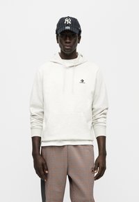 Ανοιχτό γκρι φλις φούτερ με τσέπη καγκουρό και μικρό μαύρο λογότυπο Converse, σε συνδυασμό με καρό παντελόνι και ναυτικό καπέλο με λεπτές ρίγες.