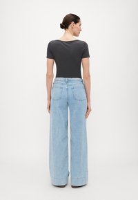 Mørk grå kortermet bodysuit kombinert med lyseblå vide jeans med baklommer og oppbrett i kanten. Glatt tekstur, avslappet passform.